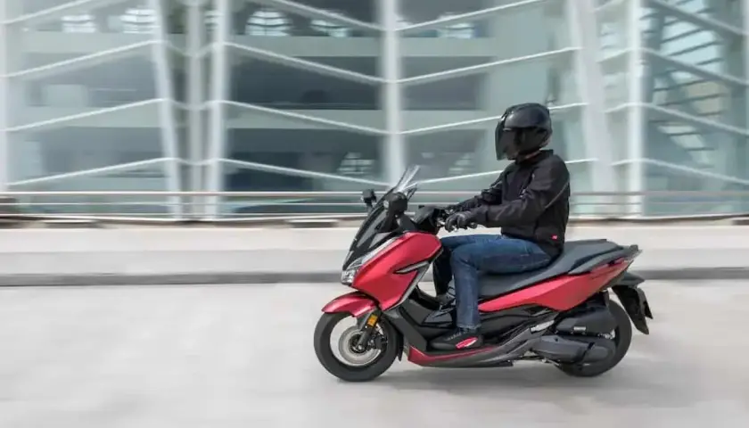 Czerwony skuter z kierowcą w kasku pędzi obok nowoczesnego budynku. To jak tuning 125 na 250, czysta moc!