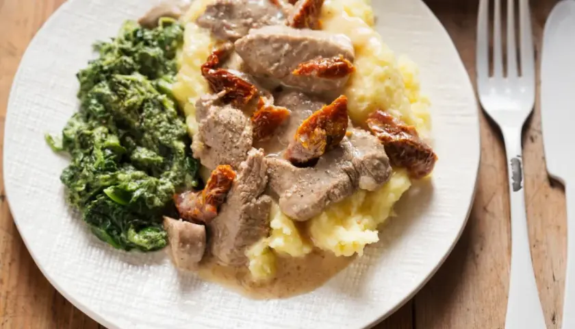 Polędwiczki z suszonymi pomidorami na kremowym purée, obok porcja szpinaku. Pyszny obiad gotowy do podania.
