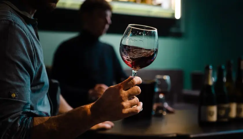 Degustacja wina w Warszawie. Mężczyzna trzyma kieliszek czerwonego wina, w tle inny uczestnik i butelki.