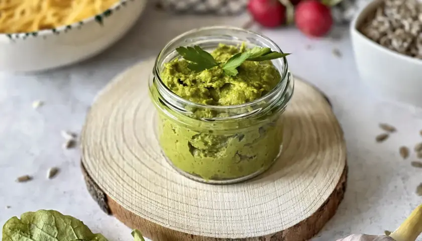 Pesto z liści rzodkiewki w słoiczku, ozdobione natką pietruszki. Obok makaron, rzodkiewki i czosnek.