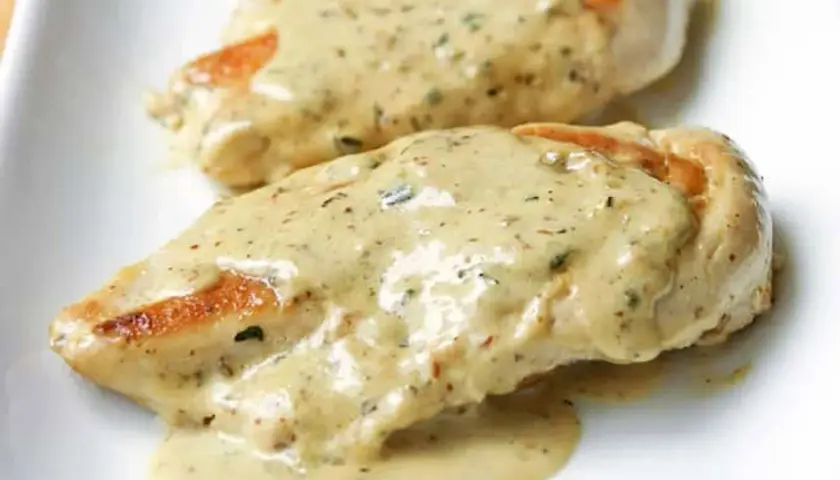 Deux morceaux de poulet à la crème, nappés d'une sauce onctueuse aux herbes, sur une assiette blanche.