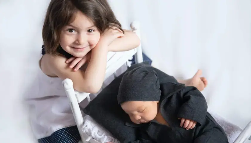 Niña sonríe mientras su hermanito duerme. Quizás ya no habrá rabietas por la llegada de un hermano.