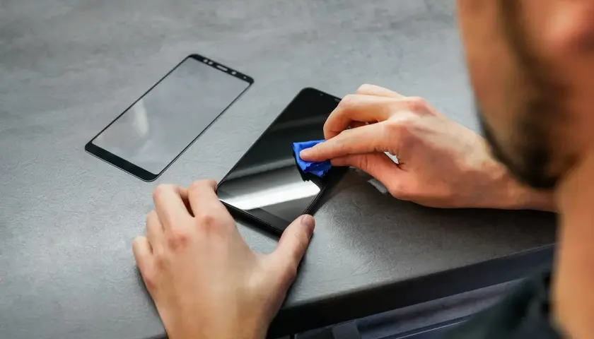 Osoba czyści ekran telefonu przed nałożeniem folii hydrożelowej. Obok leży nowa folia.