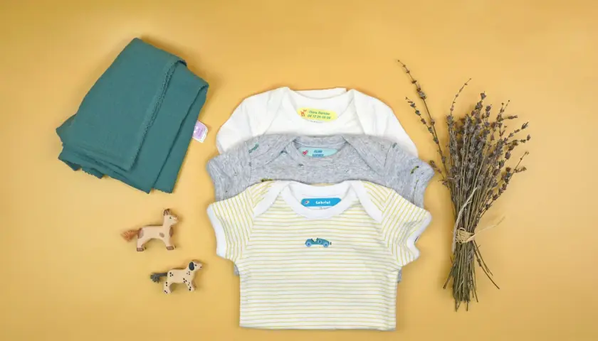 Trois bodies pour bébé avec des étiquettes personnalisées. Apprenez comment enlever une étiquette thermocollante pour réutiliser ces vêtements.