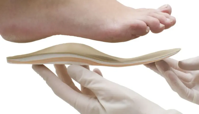 Fuß mit Plattfuß wird mit einer Einlage behandelt. Hände in Handschuhen halten die orthopädische Einlage.