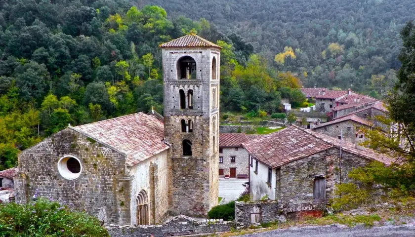 Iglesia románica y casas de piedra en un valle boscoso, ideal para explorar las rutas Camprodon.
