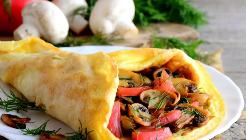 Puszysty omlet z pieczarkami i pomidorami, udekorowany koperkiem.