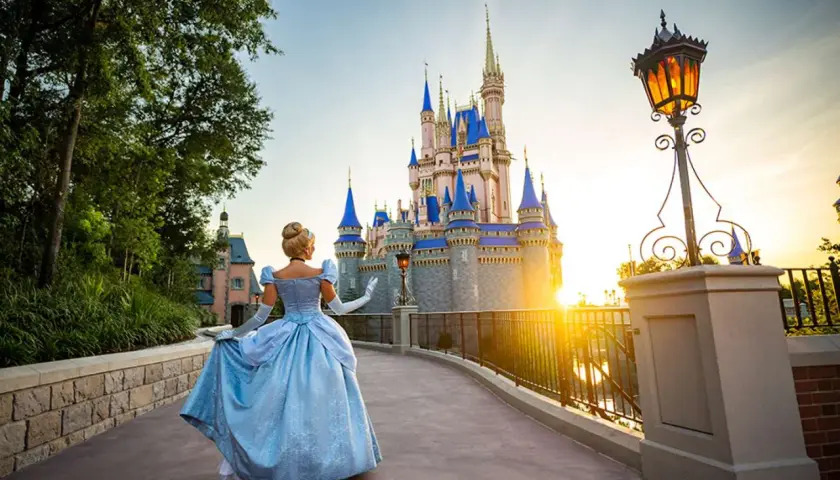 Kopciuszek w błękitnej sukni idzie w stronę zamku w Disneylandzie na Florydzie, podczas zachodu słońca.