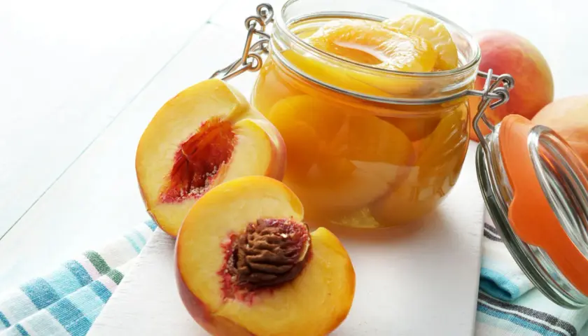 Saftige Pfirsiche in einem Glas, bereit zum Lagern. Daneben liegen frische, aufgeschnittene Früchte.