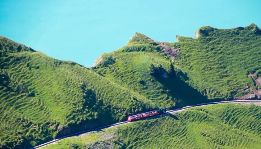 Rött tåg med passagerare på en bergssluttning vid en turkos sjö, en dröm för alla som älskar tåg interrail.
