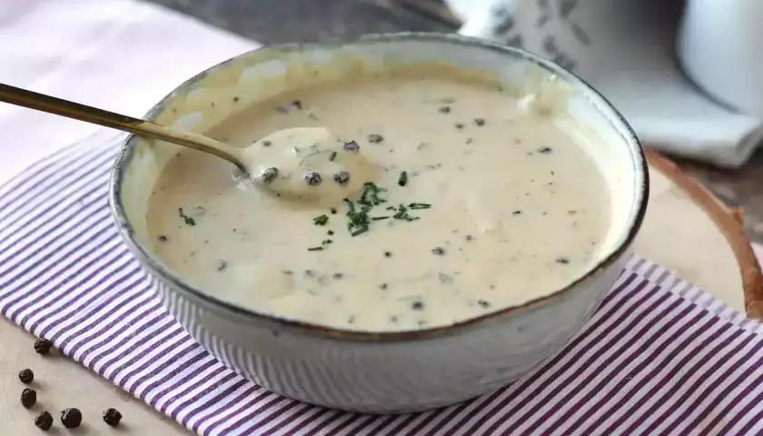 Un cuenco de cremosa salsa a la pimienta, con un toque de perejil picado y granos de pimienta negra esparcidos.