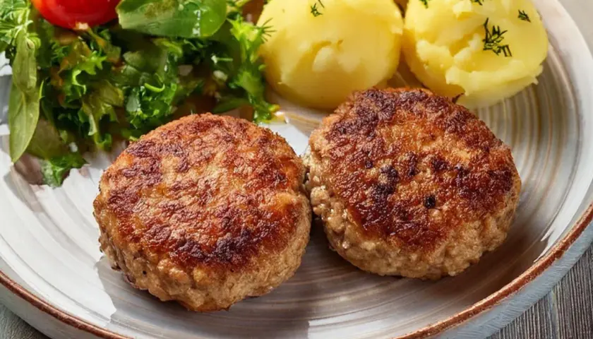 Dwa apetyczne kotlety mielone z airfryer, podane z ziemniakami i świeżą sałatką.