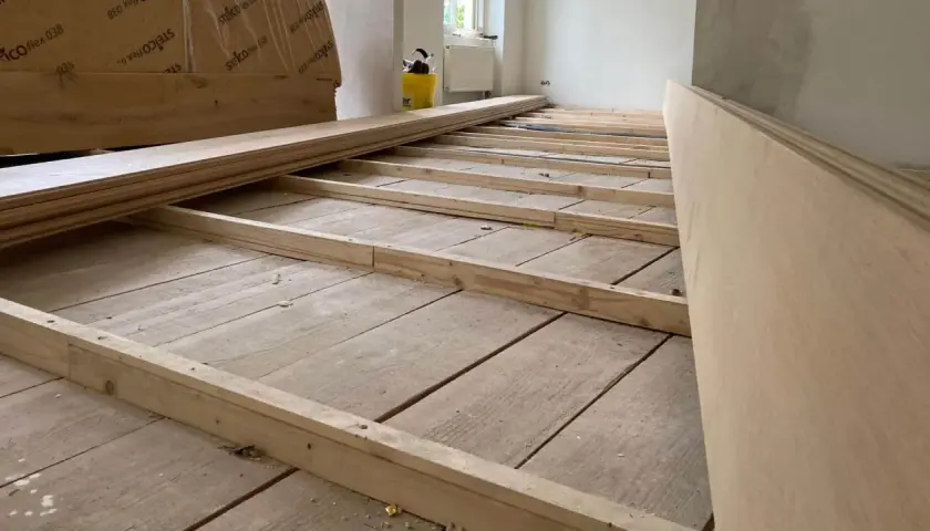 Holzbalken werden auf einem alten Holzboden verlegt, um ihn für neue Bodenplatten vorzubereiten. So kann man den Boden ausgleichen ohne Ausgleichsmasse.