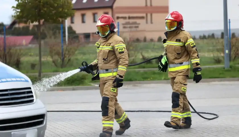 Dwóch strażaków w akcji. Jeden z nich kieruje strumień wody na pojazd. Zastanawiasz się, ile zarabia strażak?