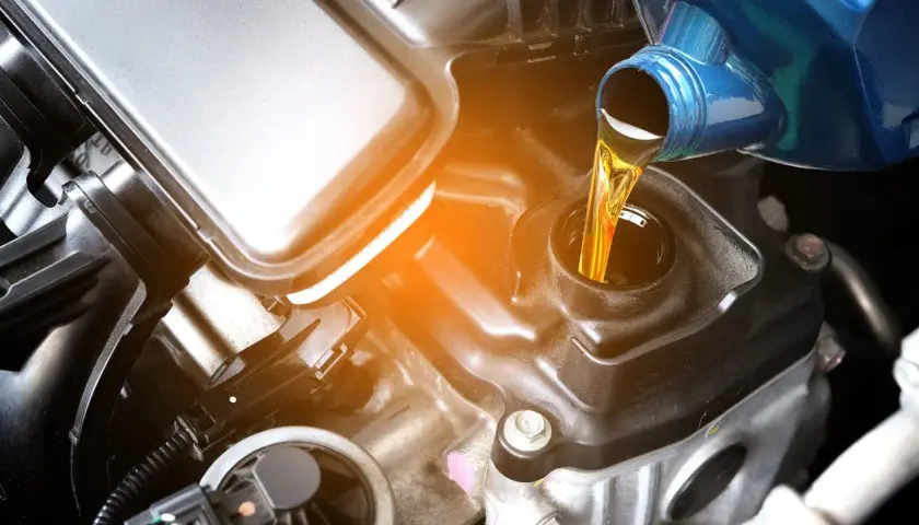 Vertiendo aceite de coche para moto en el motor. El líquido dorado fluye desde un envase azul hacia la abertura de llenado.