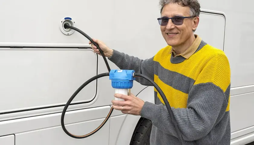 Un homme utilise un filtre à eau pour le remplissage d'eau de son camping-car. Une astuce pratique pour une eau pure en voyage.