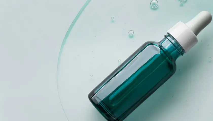 Szklana buteleczka z pipetką, zawierająca serum z kwasem mlekowym, unosząca się w przejrzystej cieczy z bąbelkami.