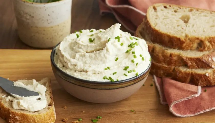 Cremiger veganer Frischkäse, garniert mit Schnittlauch, wird auf Brot gestrichen. Perfekt, um veganen Frischkäse selber machen zu lernen.