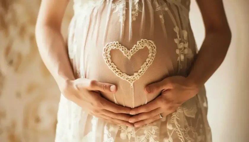 Brzuszek w 7 tygodniu ciąży, otulony koronkowym sercem. Dłonie mamy i taty czule obejmują przyszłe życie.