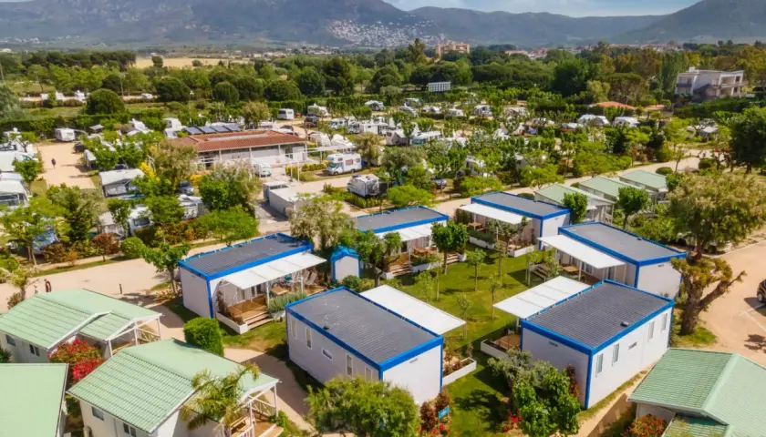 Un complejo de bungalows y caravanas para ir de camping, con montañas al fondo y un cielo azul.
