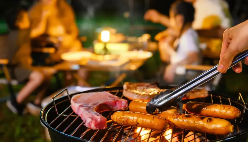 Une famille profite d'un barbecue en soirée. Des saucisses et une côte de porc cuisent sur le gril, la température de cuisson saucisse barbecue est parfaite.