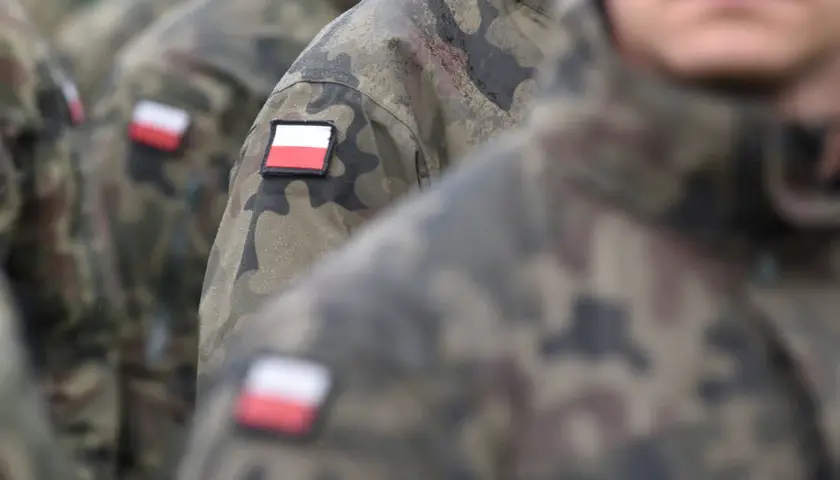 Żołnierze w mundurach moro, z polskimi flagami na ramionach, stoją w deszczu. Kategoria b wojsko.