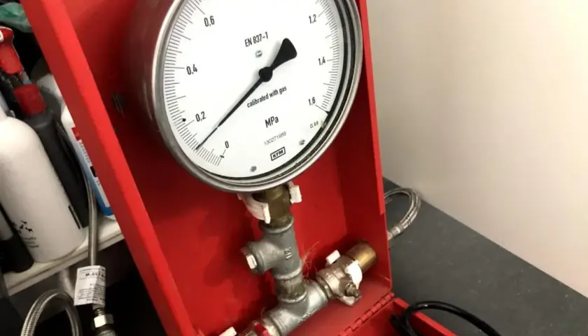 Manometr wskazuje ciśnienie podczas próby szczelności instalacji gazowej. Urządzenie jest częścią czerwonej skrzynki narzędziowej.