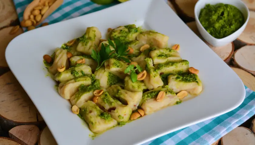 Pyszne gnocchi z pesto, posypane orzeszkami ziemnymi i udekorowane natką pietruszki. Idealne danie dla miłośników włoskich smaków.