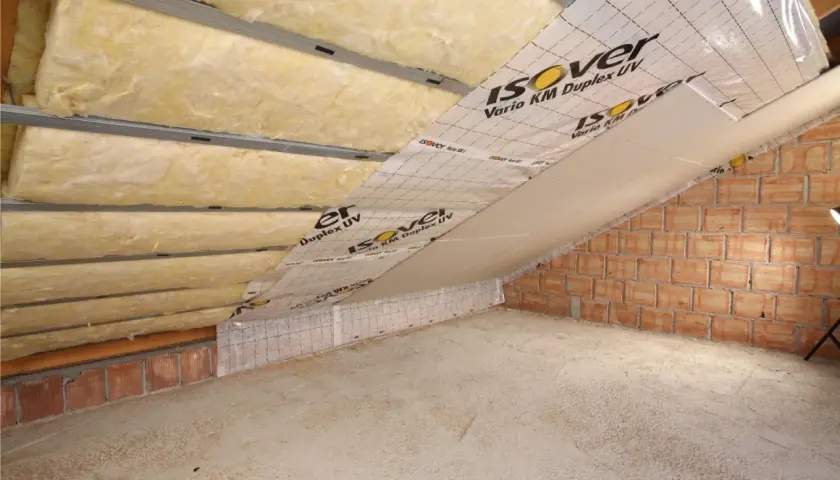 Izolacja poddasza z wełny mineralnej Isover Vario KM Duplex UV. Montaż na stelażu, widoczna folia paroizolacyjna i ściana z cegły.