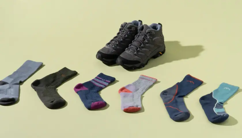Hiking boots and six pairs of colorful socks are laid out. Is wearing two pairs of socks bad? This image shows options for comfort.