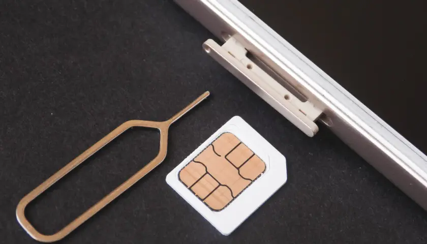 Narzędzie do otwierania tacki SIM i karta SIM obok telefonu. Dowiedz się, jak odblokować kartę SIM, aby móc korzystać z telefonu.
