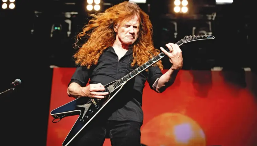 Dave Mustaine z burzą rudych włosów gra na gitarze w kształcie skrzydła.