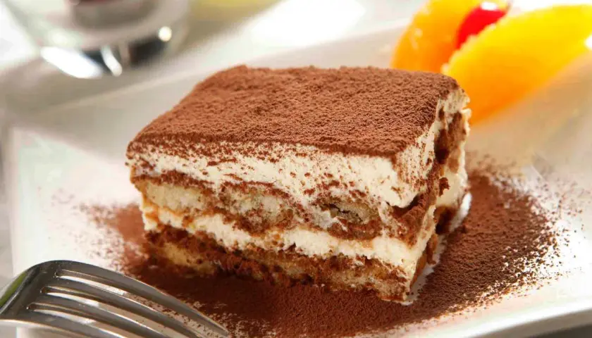Un délicieux tiramisu Kinder Bueno, saupoudré de cacao, avec des fruits en arrière-plan.