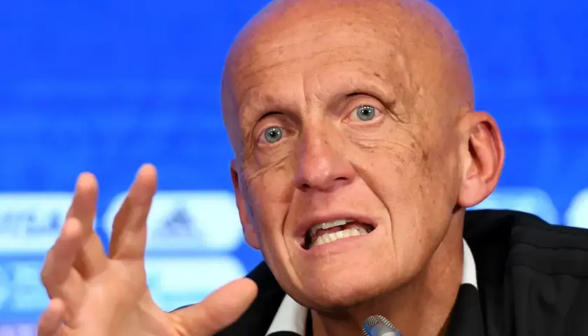 Pier Luigi Collina, znany sędzia piłkarski, przemawia do mikrofonu, gestykulując prawą ręką.