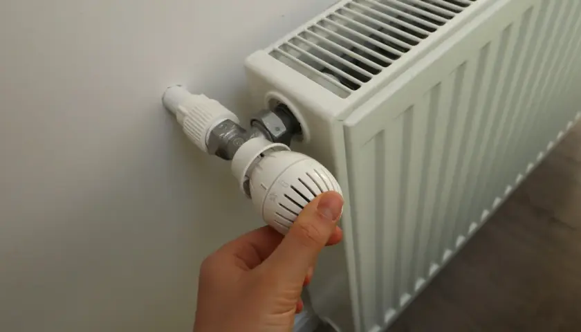 Dłoń reguluje termostat grzejnika. Sezon grzewczy od kiedy do kiedy zależy od pogody i przepisów.