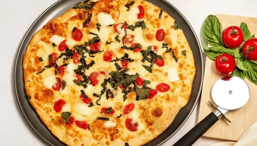 Pyszna pizza z serka wiejskiego, pomidorkami koktajlowymi i bazylią. Obok leżą świeże pomidory i nóż do pizzy.