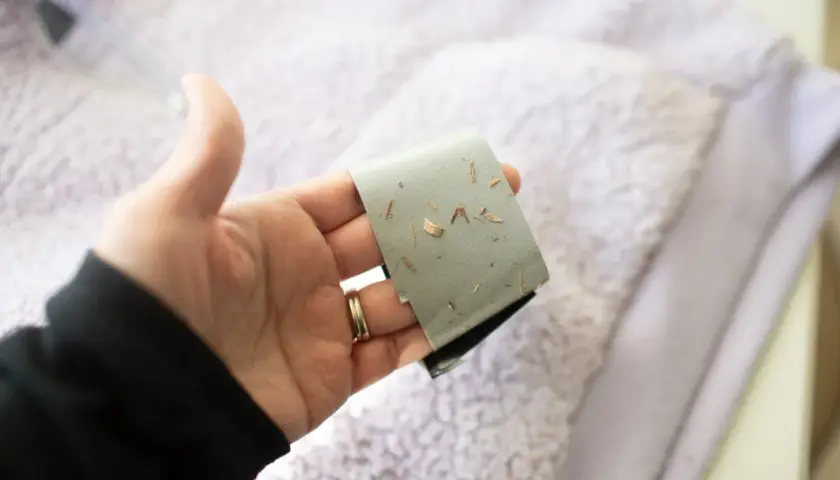 Main tenant une bande adhésive couverte de petits débris, pour montrer comment enlever un flocage sur un kway.