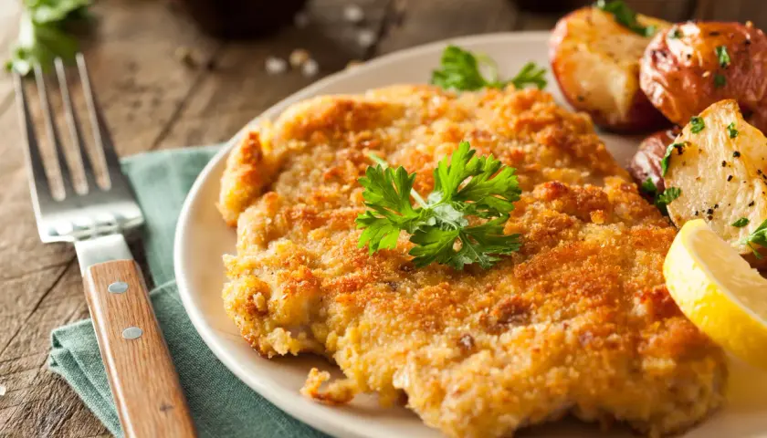 Chrupiący kotlet w złocistej panierce do mięsa, podany z pieczonymi ziemniaczkami i cytryną.