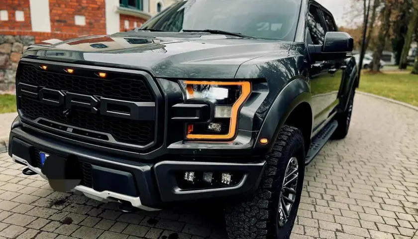 Mroczny Ford F-150 Raptor z pomarańczowymi światłami dziennymi, gotowy na przygodę.