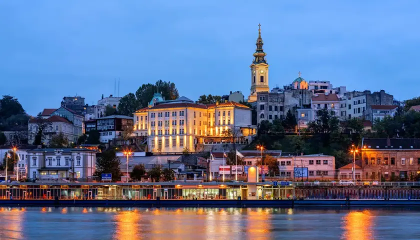Wieczorny widok na wzgórze z budynkami i kościołem, odbijający się w rzece. Stolica Serbii, Belgrad, prezentuje się malowniczo.
