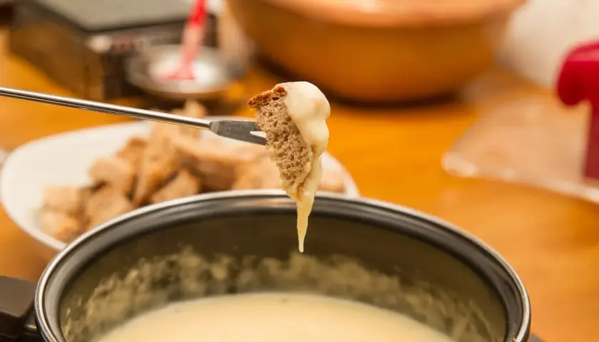 Un morceau de pain trempé dans une fondue savoyarde sans appareil. Le fromage dégouline sur la fourchette.