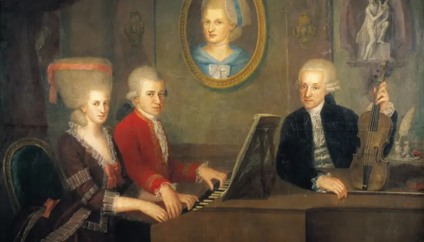 Constanze Mozart und ihre Familie musizieren. Ein Mann spielt Klavier, eine Frau sitzt daneben, ein anderer Mann hält eine Geige.