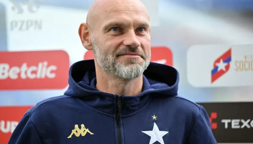 Łysy mężczyzna z siwą brodą, trener Wisły Kraków, w granatowej bluzie z kapturem z logo klubu.