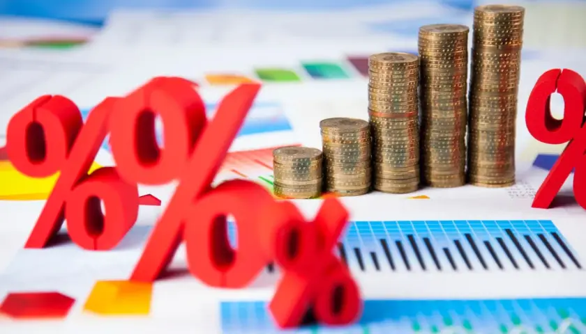 Rote Prozentzeichen und Münzstapel auf Finanzdiagrammen. Sie fragen sich, was sind Zinsen? Hier sehen Sie die Antwort visuell dargestellt.