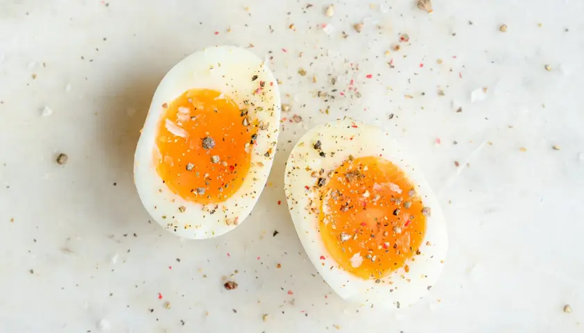 Deux moitiés d'oeuf dur trop cuit, saupoudrées de sel et de poivre, sur une surface marbrée.