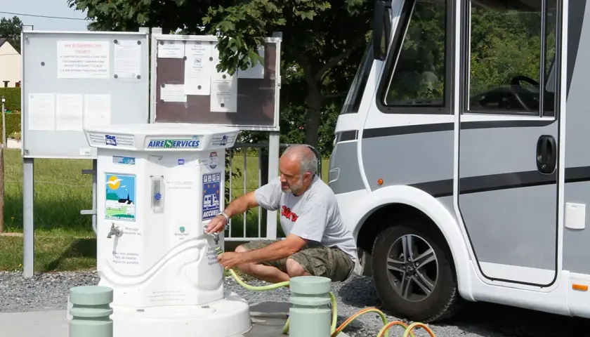 Un homme remplit un tuyau à un point d'eau pour camping-car. L'aire de services propose de l'eau potable et non potable.