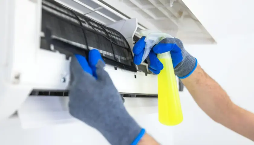 Manos enguantadas sacan filtro de aire acondicionado para limpiarlo con spray.