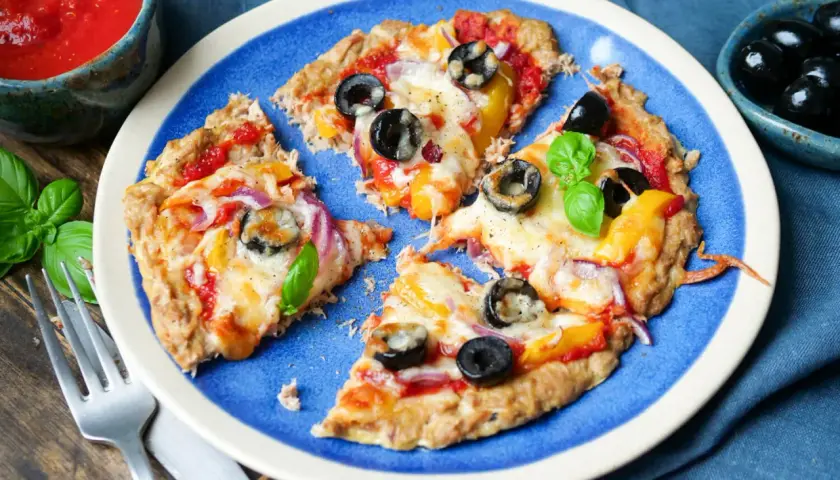 Low carb pizza thunfisch mit Oliven und Paprika auf blauem Teller, daneben eine Schale mit Tomatensauce und frischem Basilikum.
