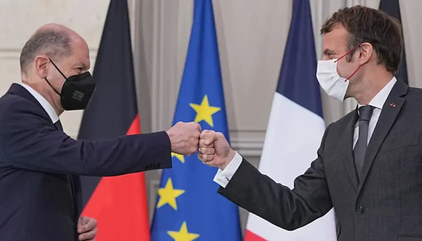 Olaf Scholz und Emmanuel Macron stoßen Fäuste vor den Flaggen von Deutschland und Frankreich.