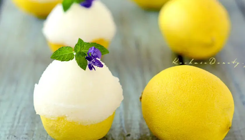 Orzeźwiający sorbet cytrynowy podany w wydrążonych cytrynach, udekorowany miętą i fioletowym kwiatkiem.